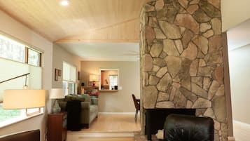 Una sala de estar con chimenea de piedra, techo de madera y vista al comedor.
