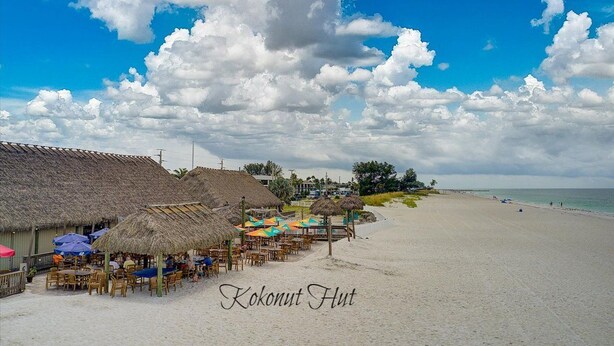 Ein Restaurant direkt am Strand mit Reetdächern und Terrassenplätzen, gelegen an einem Sandstrand mit Blick auf den Ozean.
