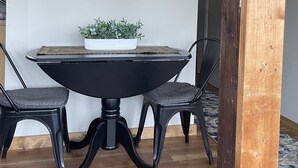 Ein Essbereich mit einem runden Tisch, zwei Stühlen, einem Topf mit Pflanze und einem an der Wand befestigten Fernseher.
