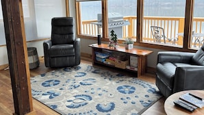 Ein gemütliches Wohnzimmer mit Kamin, einer Ledersofa, einem Couchtisch und einem großen Fenster mit Blick auf eine Terrasse.