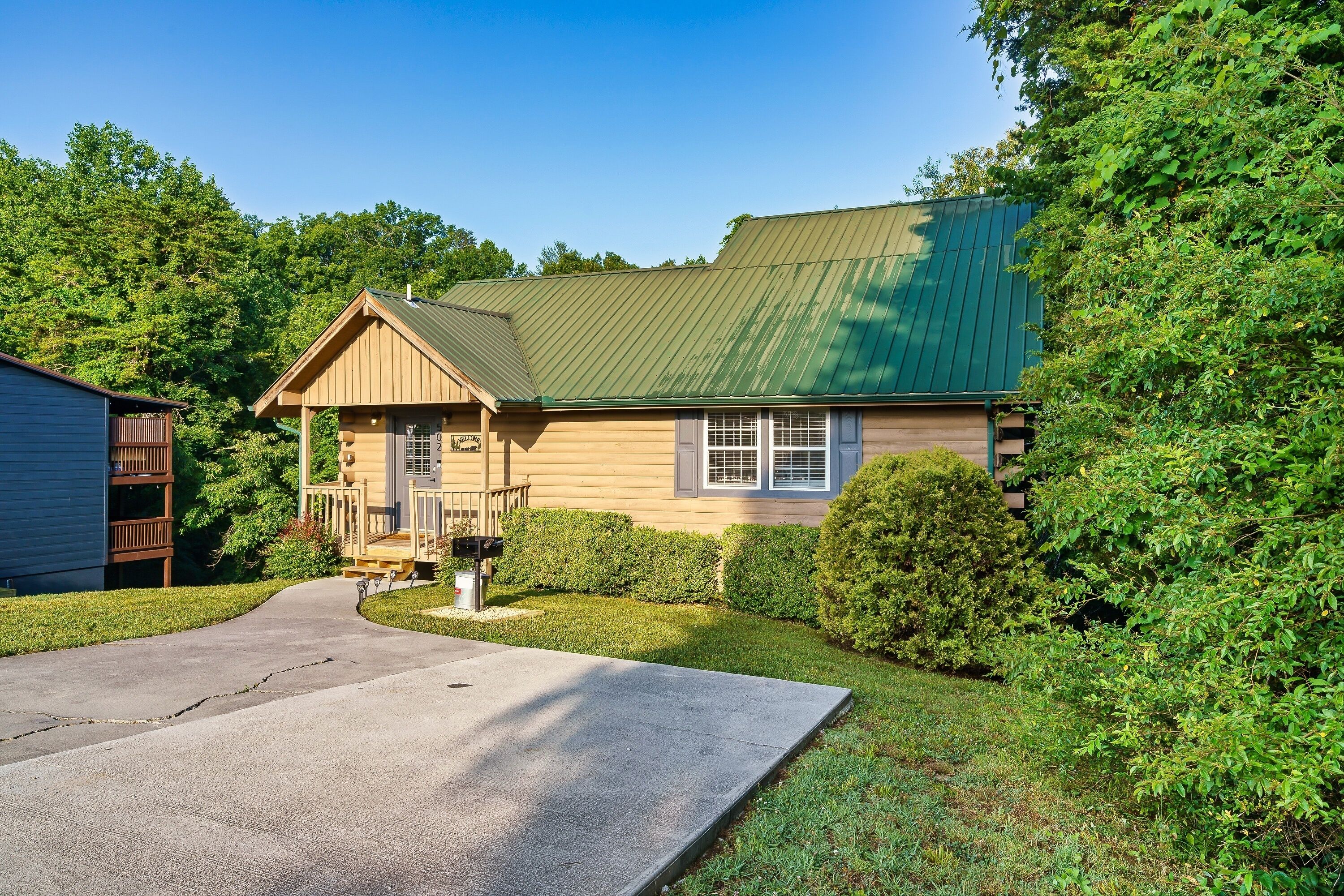 A two-story house with a green roof, a front porch, and a driveway leading to the entrance.