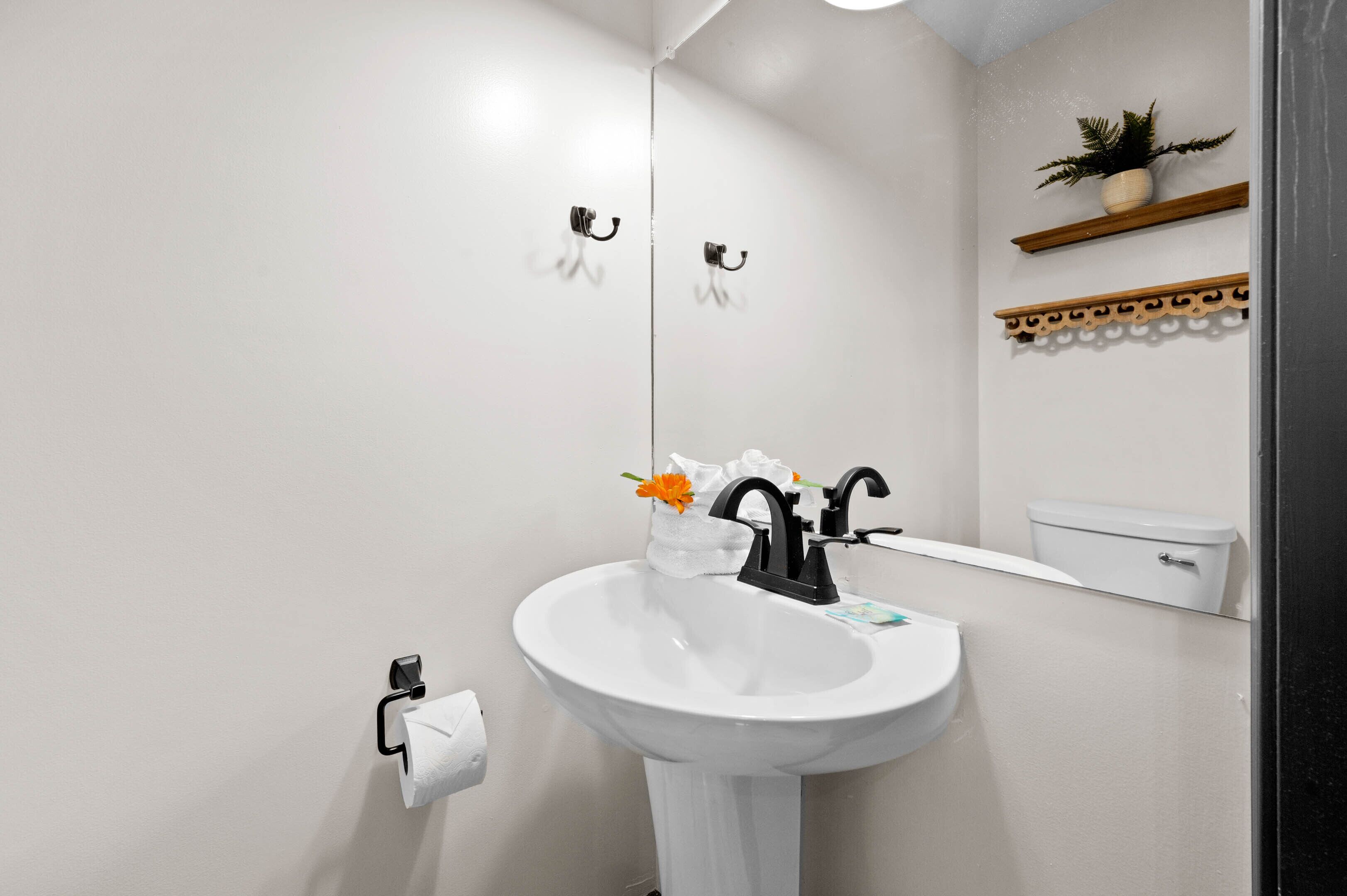 Un baño con un lavamanos blanco, un grifo negro y un espejo encima. Se ve un inodoro al fondo.