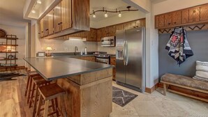 Una cocina moderna con armarios de madera, una isla grande con taburetes, un refrigerador de acero inoxidable y un microondas.
