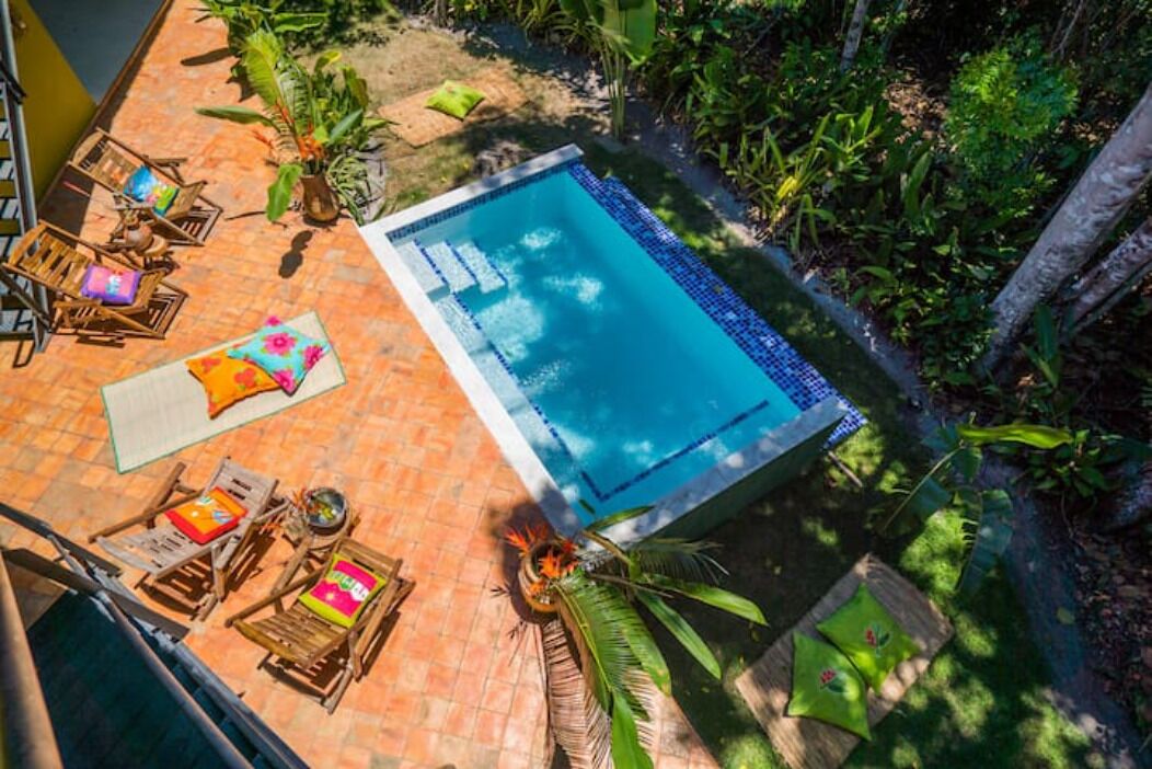 Une piscine sur le toit, bordée de carreaux, entourée de chaises longues en bois et d’une petite table.