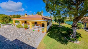 A yellow house with a tiled roof, a stone patio, and potted plants.