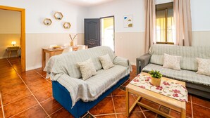 A living room with a blue sofa, a grey sofa, a wooden coffee table with a floral table runner, and a small side table with a lamp.