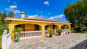 A yellow house with a tiled roof, a stone-paved courtyard, and a white railing.