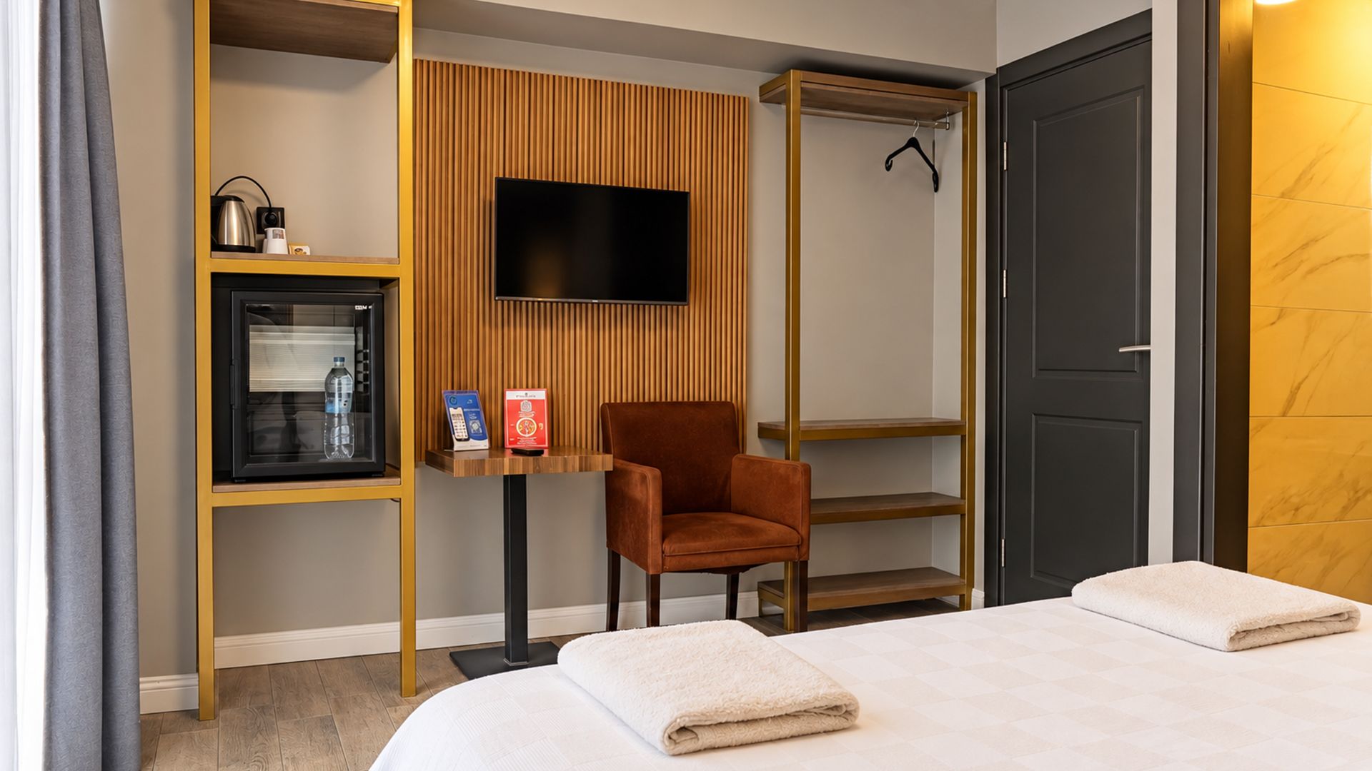 Ein Hotelzimmer mit Bett, Stuhl, Fernseher, Minibar und Kleiderschrank.