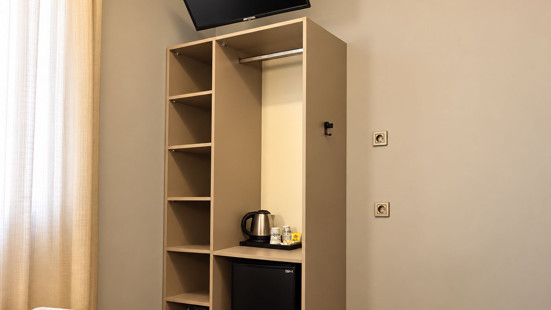 Uma cozinha compacta com cafeteira, mini geladeira e TV de tela plana instalada acima das prateleiras.
