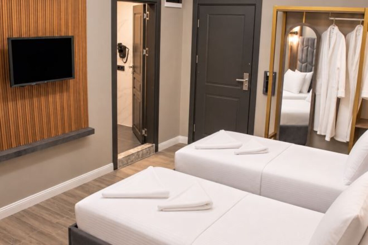 Ein Hotelzimmer mit zwei Betten, einem an der Wand montierten Fernseher, einer Tür zu einem Badezimmer und einem Kleiderschrank mit Bademänteln.