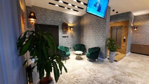 Un hall d’entrée avec des fauteuils verts, une petite table ronde et un écran de télévision.