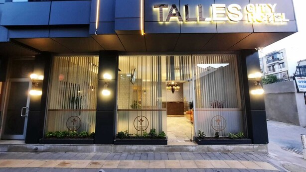 Entrada de hotel com design moderno, destacando grandes janelas de vidro e um interior visível com um lustre.