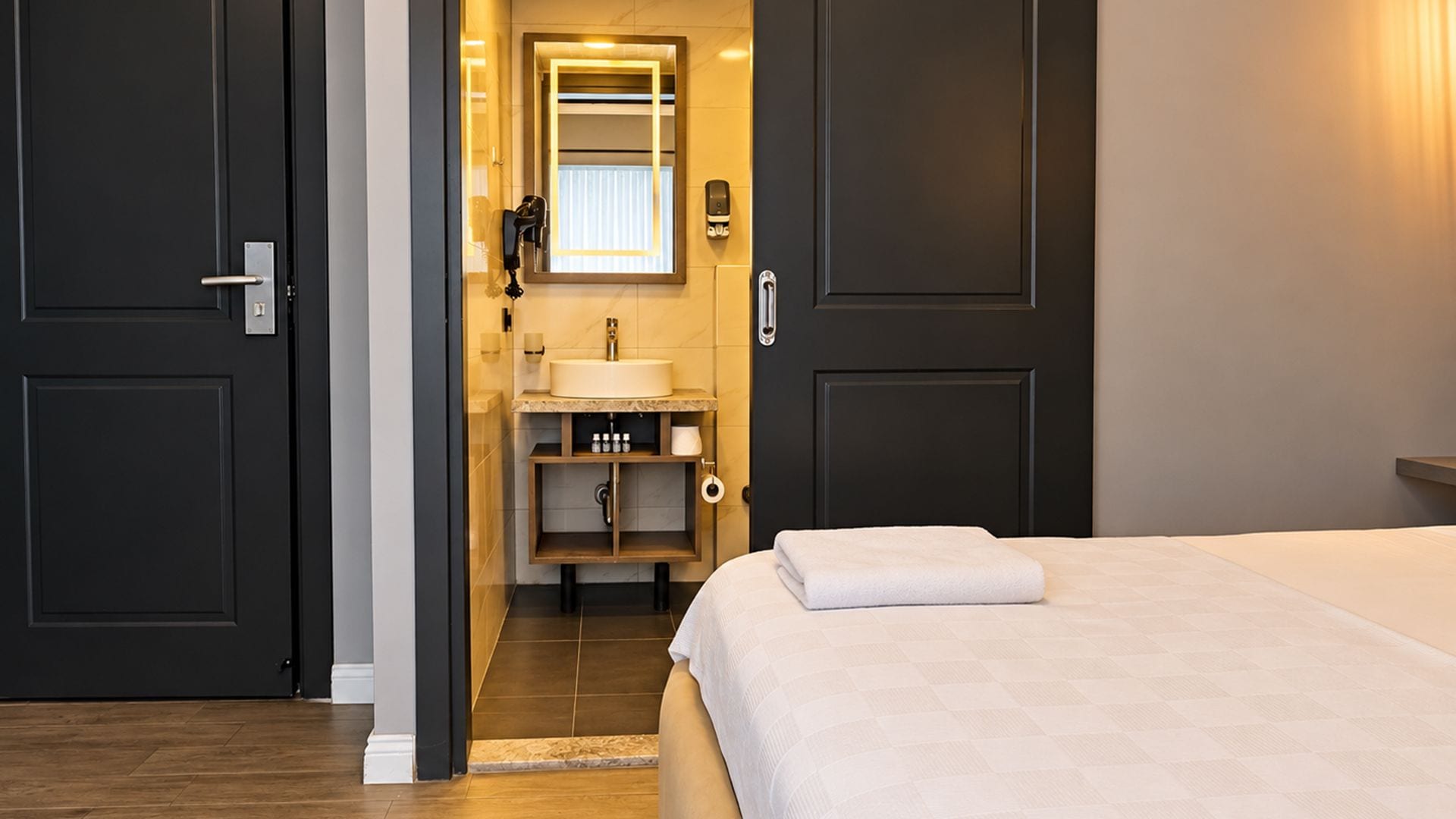 Et hotelværelse med seng, badeværelse med håndvask og spejl.