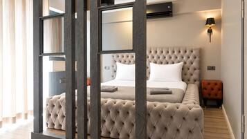 Een slaapkamer met een gestapeld hoofdeinde, een bed met witte lakens, een nachtkastje, een lamp en een kleine oranje fauteuil.