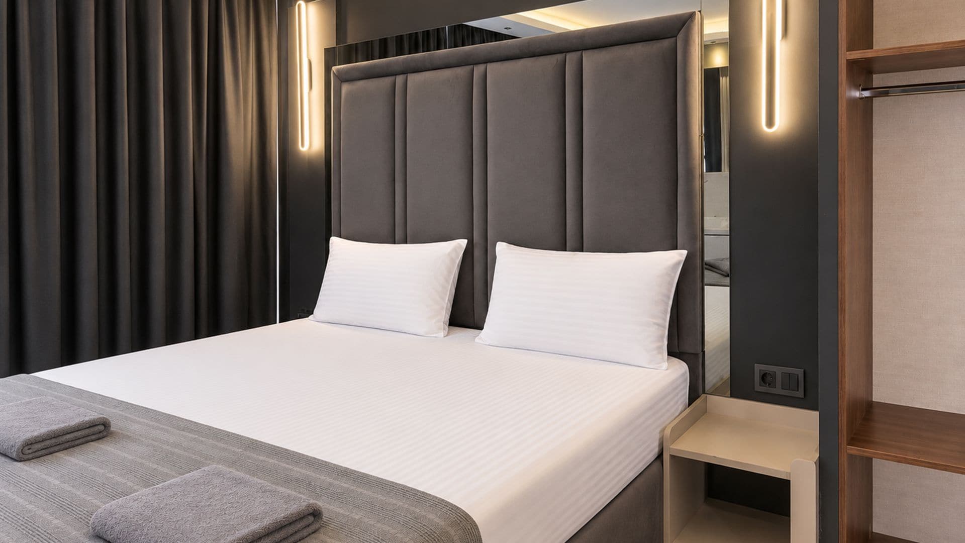 Una habitación de hotel moderna con una cama grande, una mesita de noche y un armario empotrado.