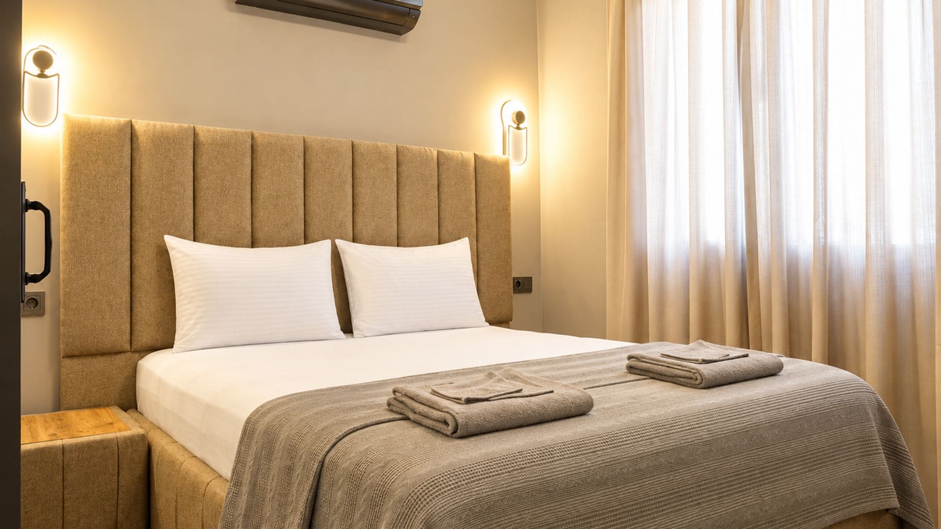 A hotel room with a large bed, two bedside lamps, a window with curtains, and a wooden nightstand.