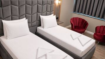 Een hotelkamer met twee bedden, een grijze hoofdbord, rode stoelen en een raam met gordijnen.