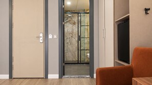 Habitación de hotel con puerta corredera que da a un baño, un televisor y piso de madera.