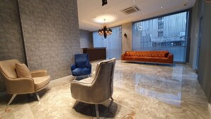 A modern interior with a sofa, two armchairs, a chandelier, and a large window.