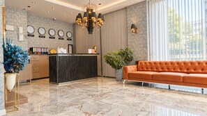 En hotellobby med en receptionsdisk, en stor kristallkrona, en soffa och en krukväxt.