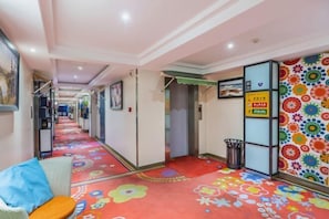 Corredor de hotel com carpete floral colorido, uma lixeira e uma parede com padrão circular colorido.