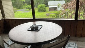 Une table ronde avec un plateau rempli de tasses, une chaise et une vue sur une maison par la fenêtre.