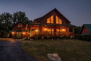 A large log cabin with a porch and multiple windows, surrounded by a well-maintained lawn and trees.