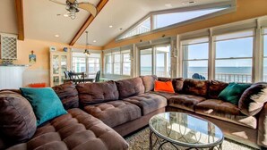 A spacious living area with a large brown leather sofa, a glass coffee table, and large windows offering a view of the ocean.