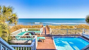 A wooden deck with lounge chairs and a pool, overlooking a beach and ocean.