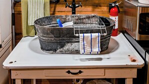 A rustic kitchen with a wooden interior, a window with curtains, a sink with a metal basin, a fire extinguisher, and a sign on the wall. - Fabulous Shack in the heart of Tellico Plains... (Tellico Plains)