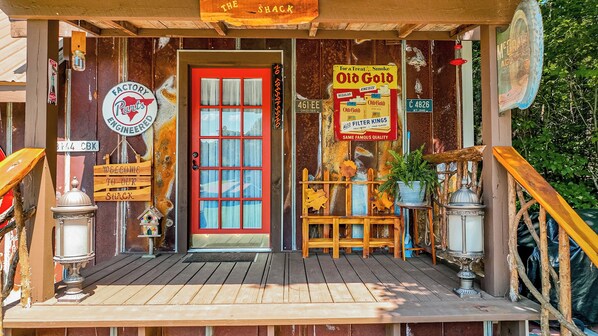 A rustic wooden building with a red door, vintage signs, and a wooden porch.