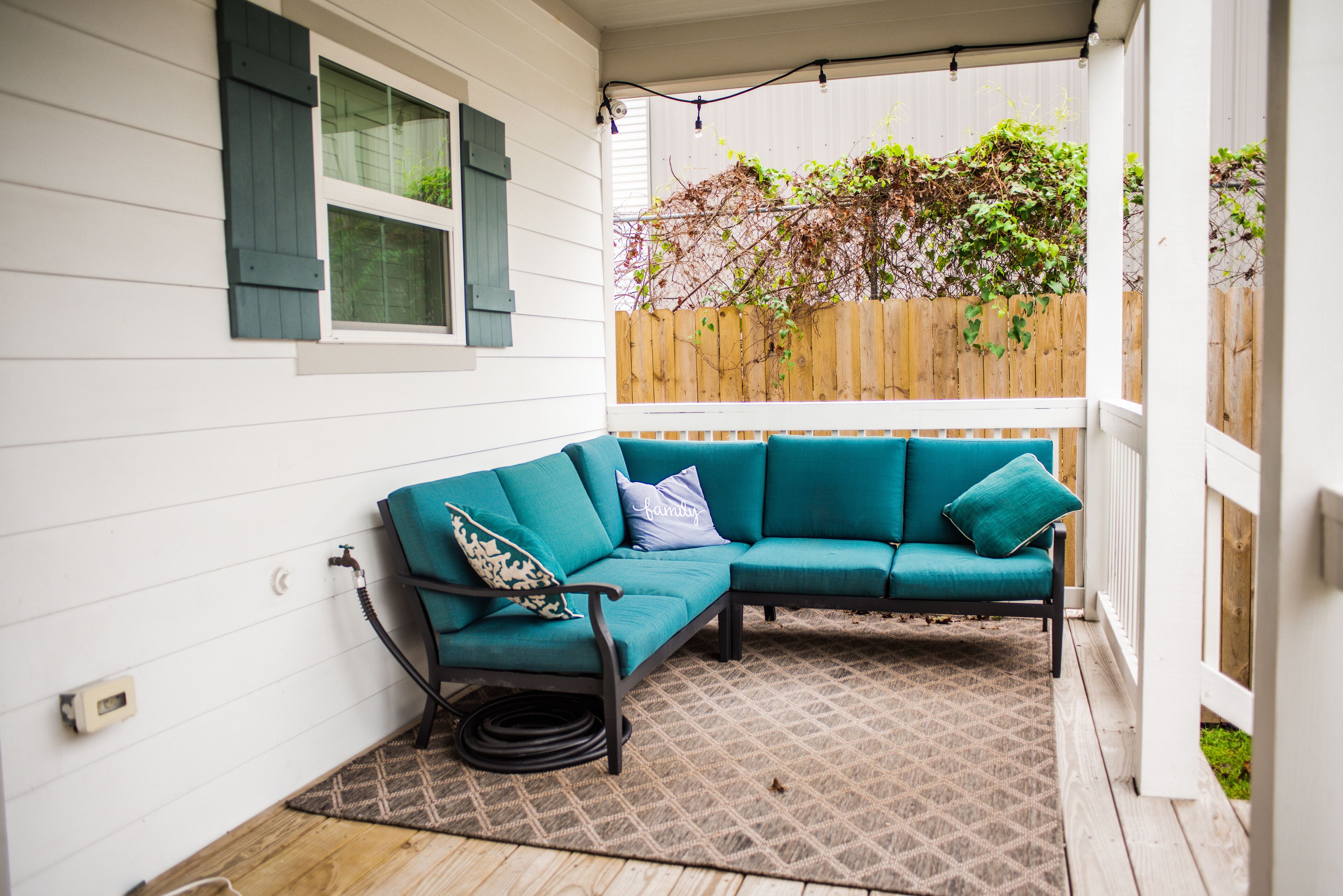 Un petit patio aménagé dans un coin, avec un canapé de couleur turquoise, un tapis à motifs et une clôture en bois.
