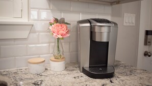 Une cuisine équipée d’une machine à café, d’un vase rempli de fleurs et d’un plan de travail en marbre.