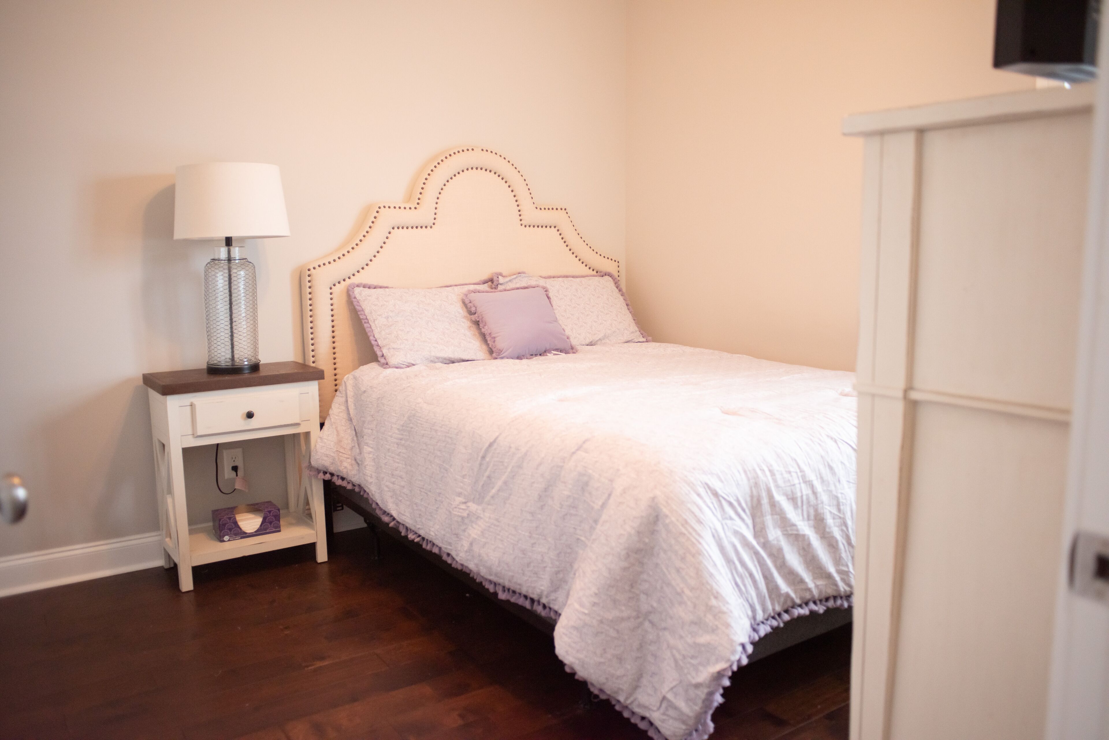 A bedroom with a bed, a nightstand with a lamp, and a wardrobe.