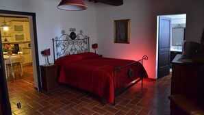 A bedroom with a red bedspread, a metal headboard, a hanging lamp, and a painting on the wall. - La Petronilla Montepetriolo - Apartment Delight (Monte Petriolo)