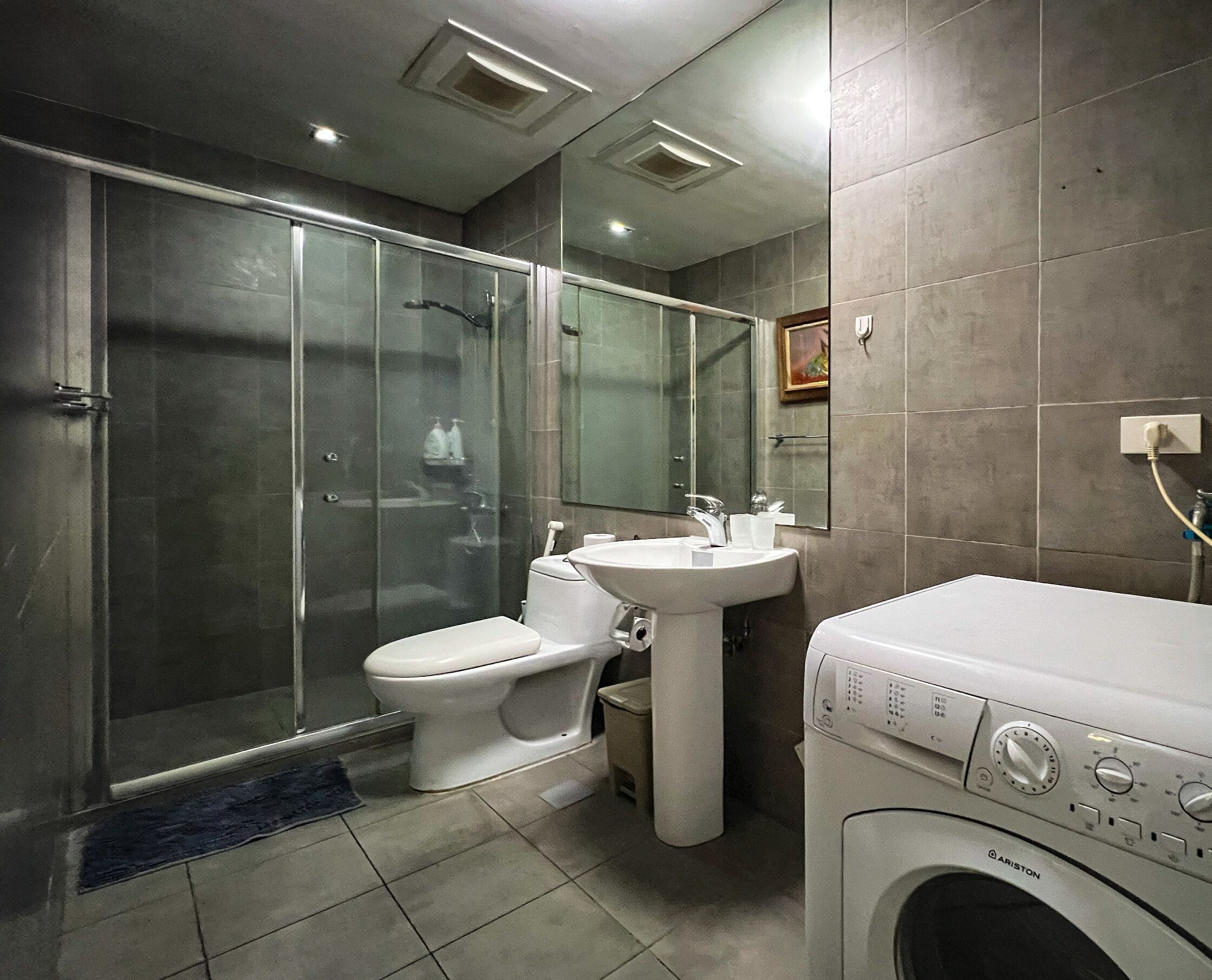 A modern bathroom with a glass-enclosed shower, a toilet, a sink, and a front-loading washing machine.