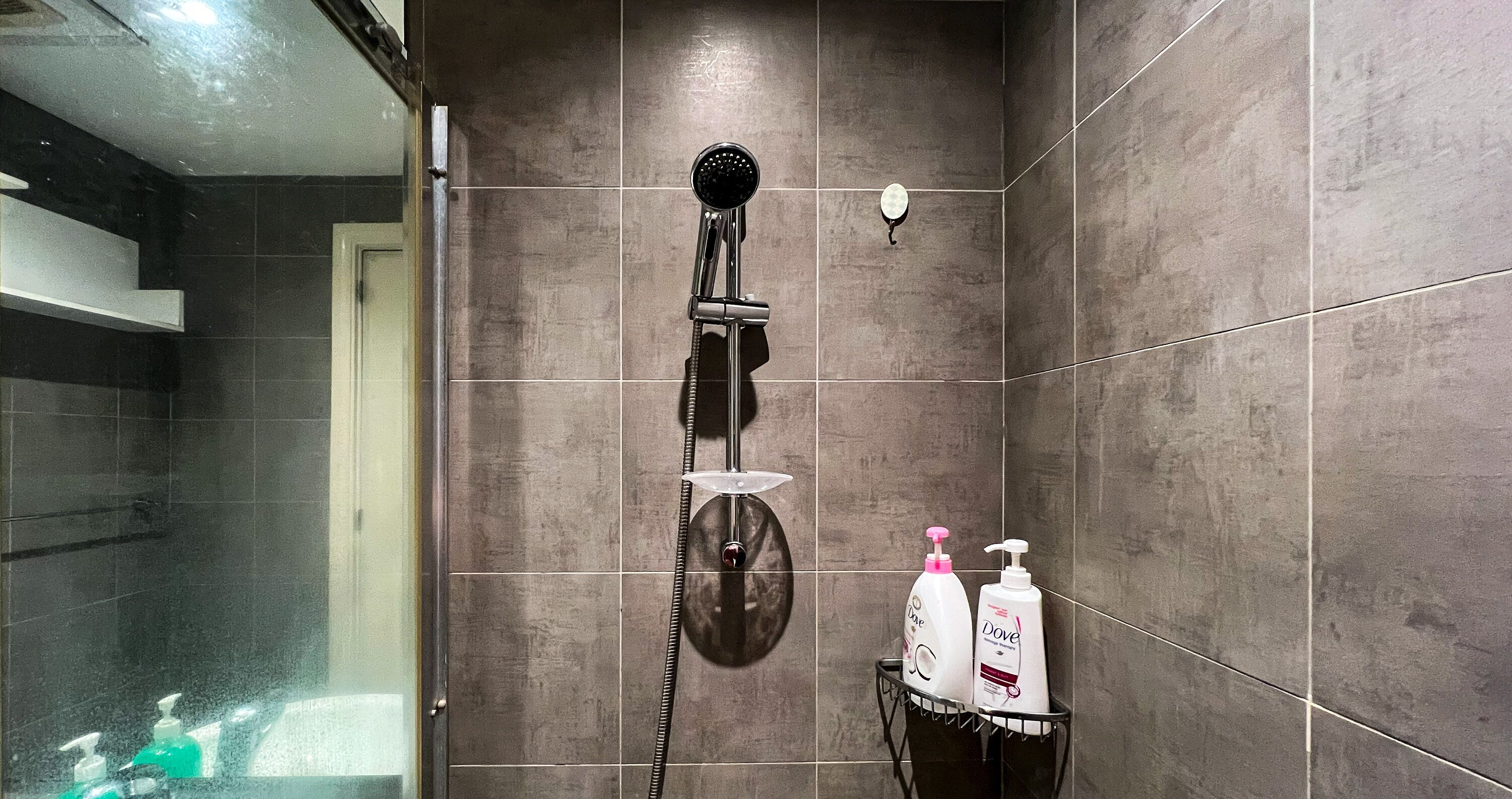 A shower area with a handheld showerhead, a glass-enclosed shower, and two Dove shampoo bottles on a black tray.