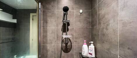 A shower area with a handheld showerhead, a glass-enclosed shower, and two Dove shampoo bottles on a black tray.