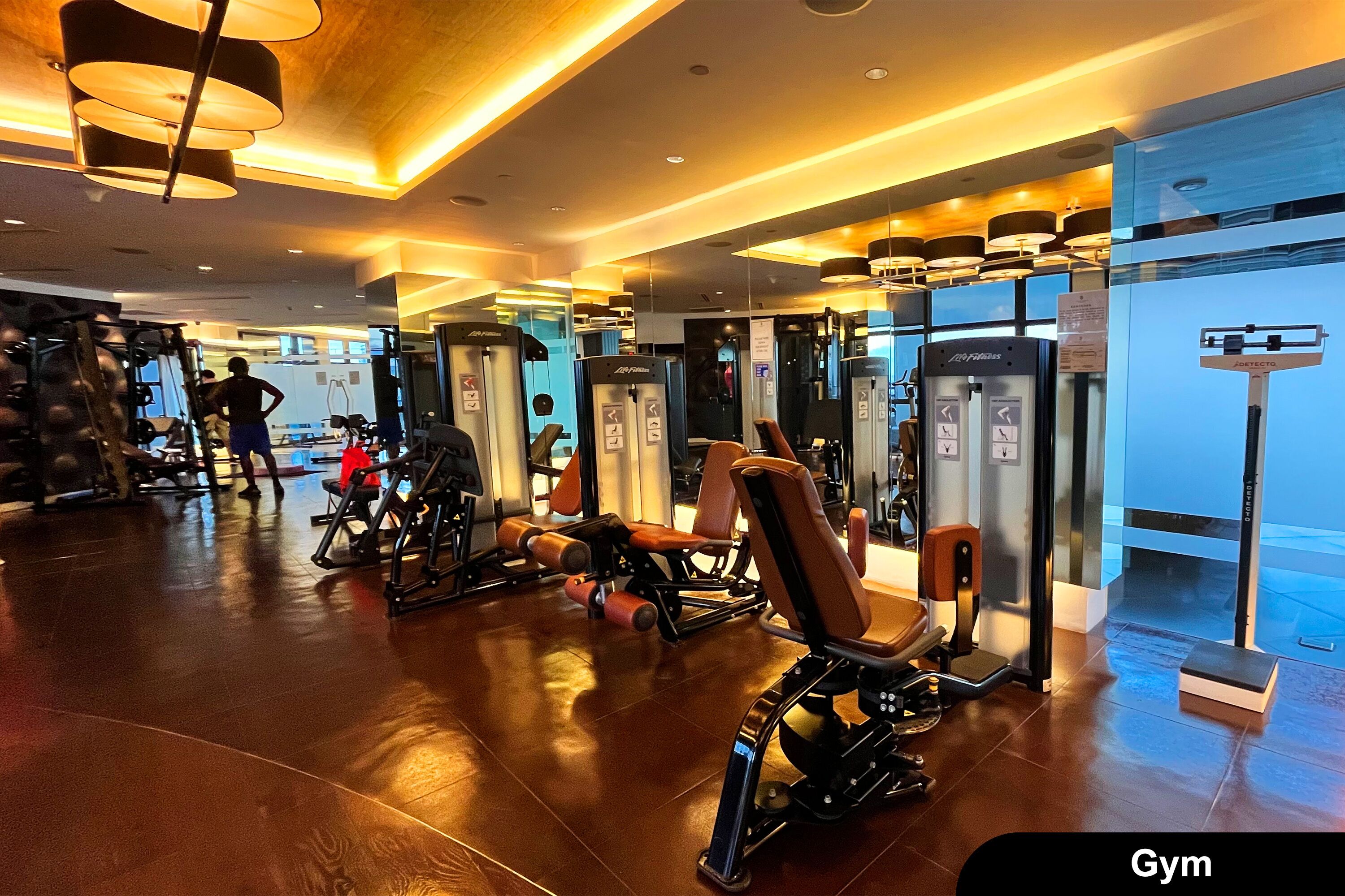 Une salle de sport équipée de divers appareils d’exercice, dotée d’un plancher en bois et d’un design de plafond moderne.
