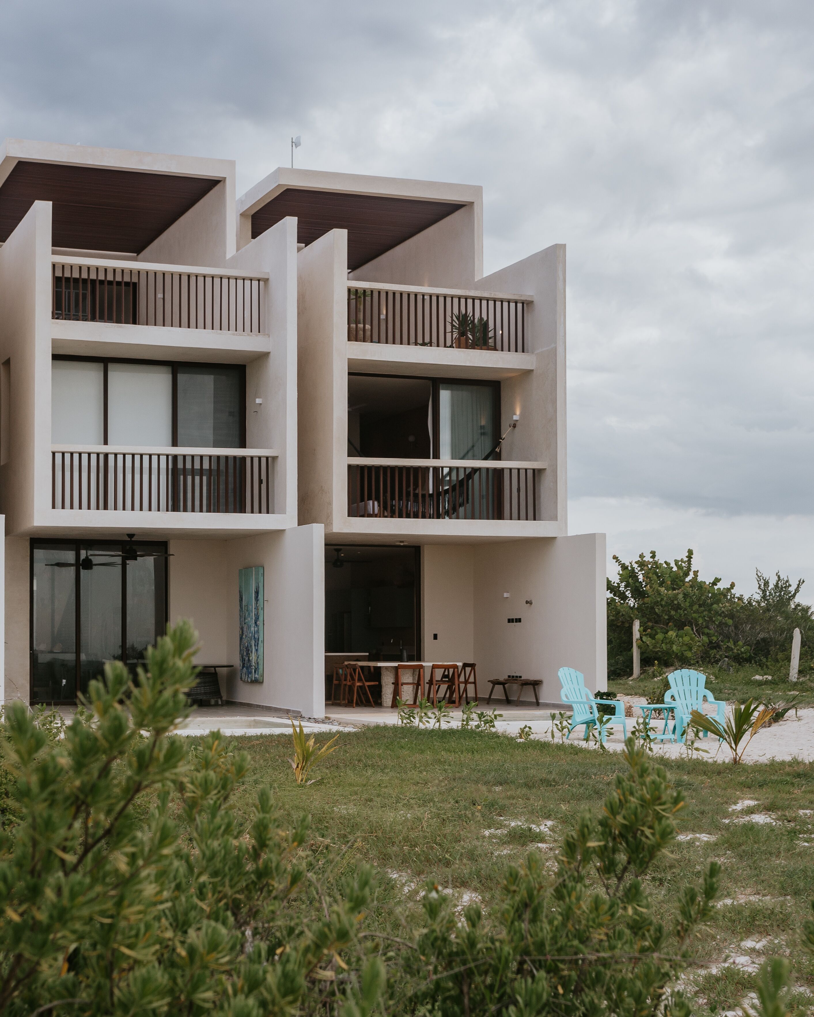 Un edificio moderno de varios pisos con balcones, un comedor con mesas al aire libre y vistas del paisaje circundante.