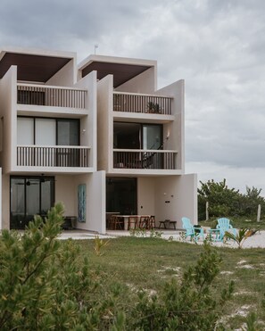 A modern multi-story building with balconies, a dining area with outdoor seating, and a view of the surrounding landscape. - Punta de Vista (Dzemul)