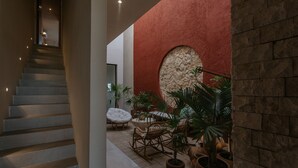 Una escala que condueix a una zona d'estar amb una paret vermella, un arc de pedra i plantes en testos.