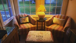 A cozy living room with striped sofas, a small table with a lamp, and a bench with a floral cushion.