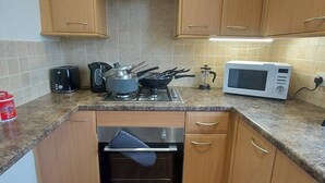 Een kleine keuken met houten kastjes, een gasfornuis, een magnetron en een broodrooster.
