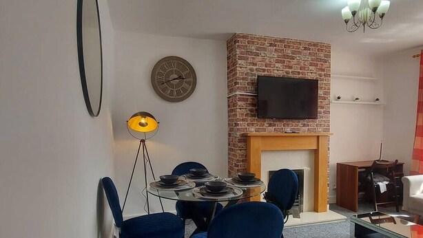 Een eetruimte met een open haard van baksteen, een flatscreen televisie erboven en een ronde tafel met blauwe stoelen.
