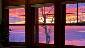 A room with large windows offering a view of a sunset over a body of water.