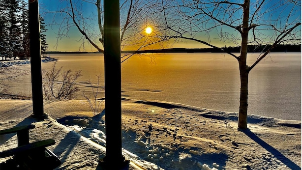 A covered outdoor area with a view of a frozen lake and bare trees.