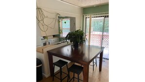 Una cocina con una mesa de madera y dos taburetes, una ventana con persianas y una planta en maceta.