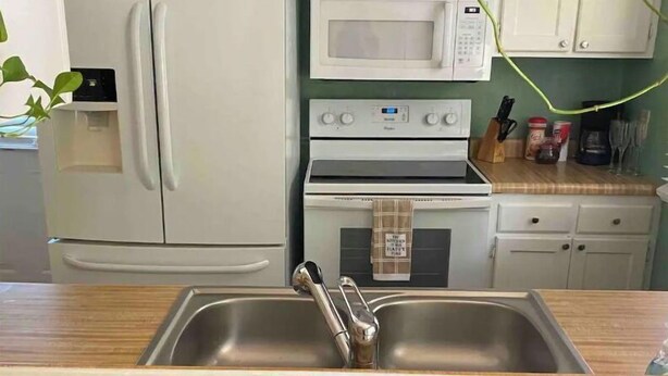 Una cocina con gabinetes blancos, microondas, estufa y pileta.