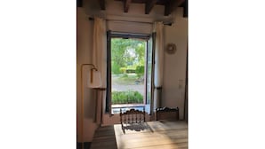 Une pièce avec un plancher en bois, un lit doté d’une tête de lit, une fenêtre avec des rideaux et une vue sur un jardin.
